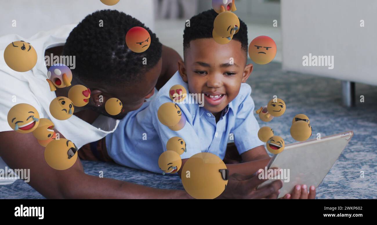 Image of emoticons over happy african american father and son using tablet Stock Photo