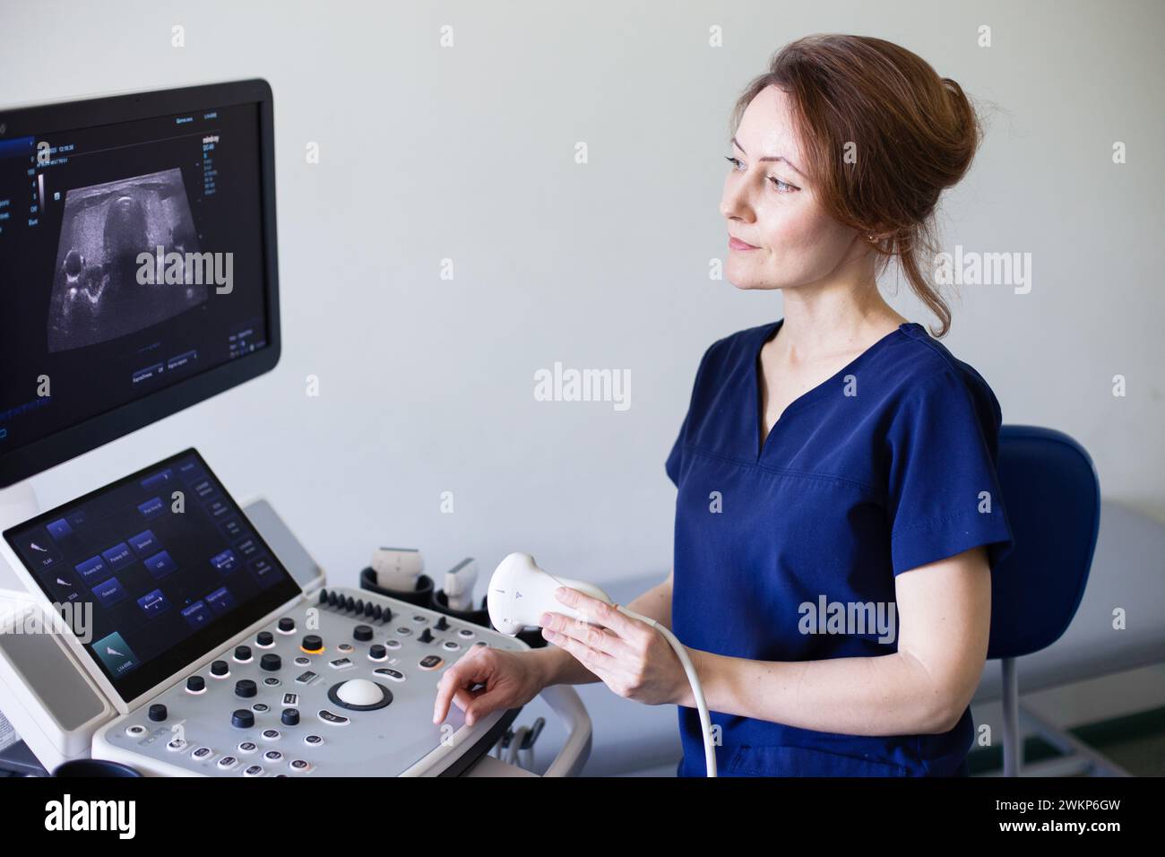 Doctor woman in uniform sitting in office in hospital with ultrasound diagnostic machine equipment and ready to examine patients doing ultrasound of t Stock Photo