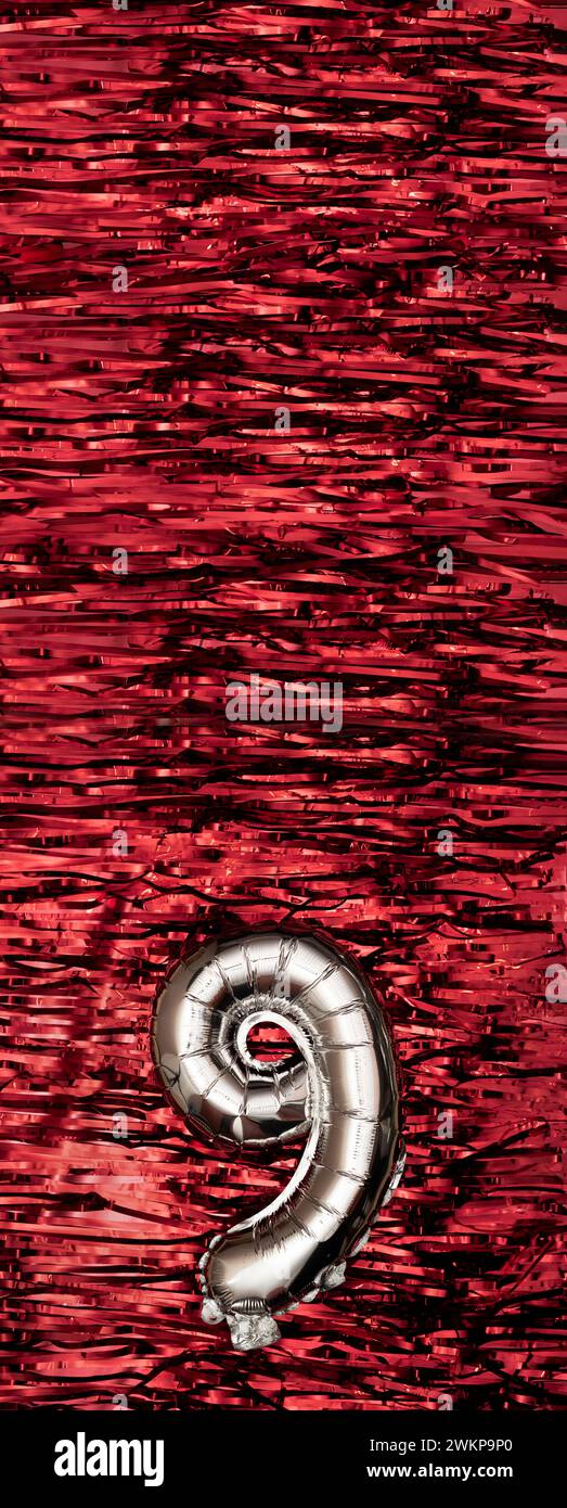 Silver foil balloon number number 9 on a background of red tinsel