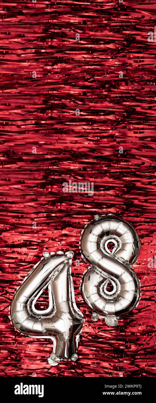 Silver foil balloon number number 48 on a background of red tinsel decoration. Birthday greeting card, inscription forty-eight. Anniversary event Stock Photo