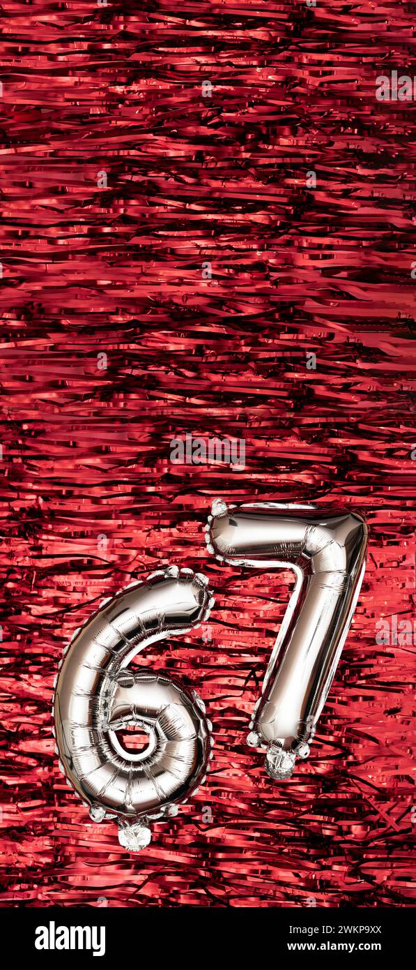 Silver foil balloon number 67 on a background of red tinsel decoration