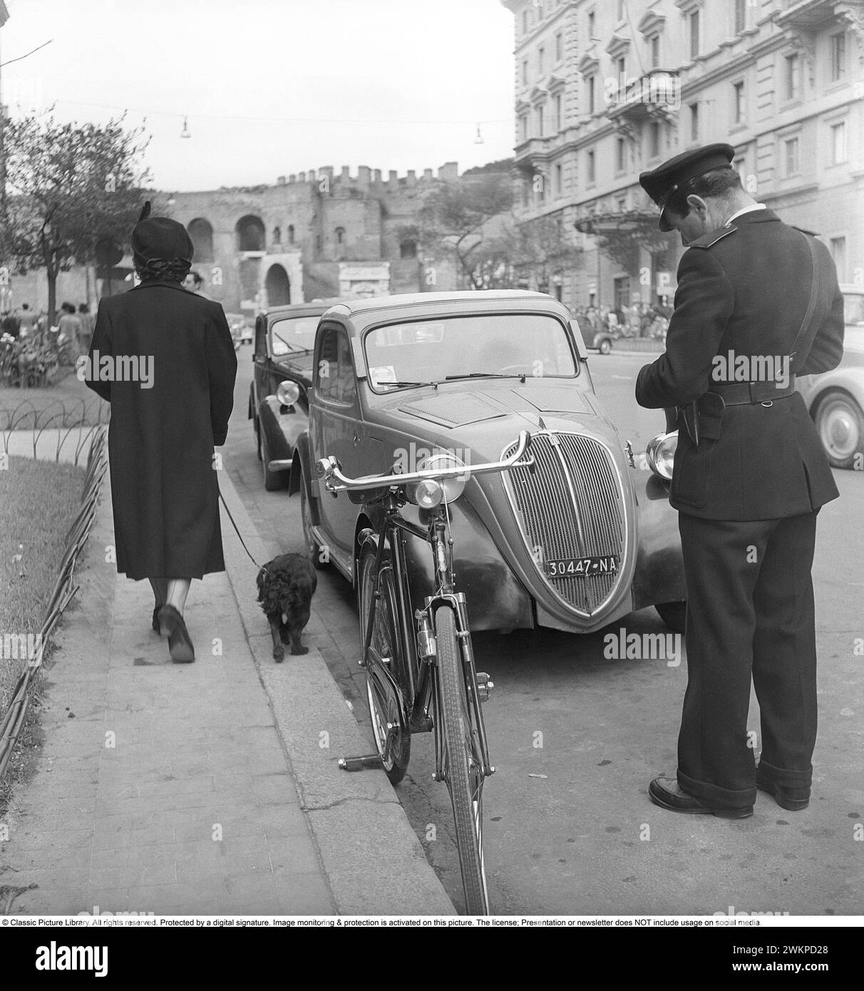 In Italy in the 1950s. A traffic warden in the street who writes a ticket for the parked car. Milan Italy 1950. Photo Kristoffersson Ref DV19 *** Local Caption *** © Classic Picture Library. All rights reserved. Protected by a digital signature. Image monitoring & protection is activated on this picture. The license; Presentation or newsletter does NOT include usage on social media. Stock Photo