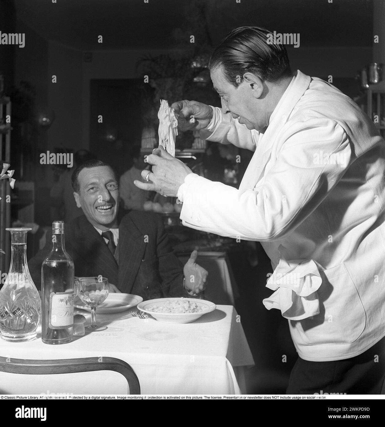 In Italy in the 1950s. A waiter at the table holds the newly cooked pasta and showing it to the guest at the restaurant. Milan Italy 1950. Photo Kristoffersson Ref AY23-12 *** Local Caption *** © Classic Picture Library. All rights reserved. Protected by a digital signature. Image monitoring & protection is activated on this picture. The license; Presentation or newsletter does NOT include usage on social media. Stock Photo