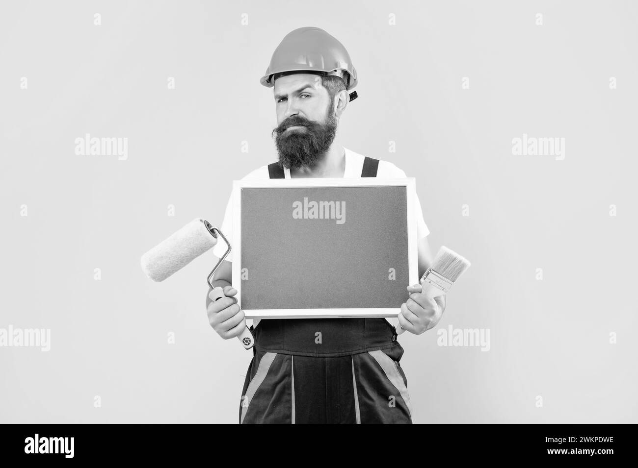 man painter in helmet and work clothes hold paint roller brush and