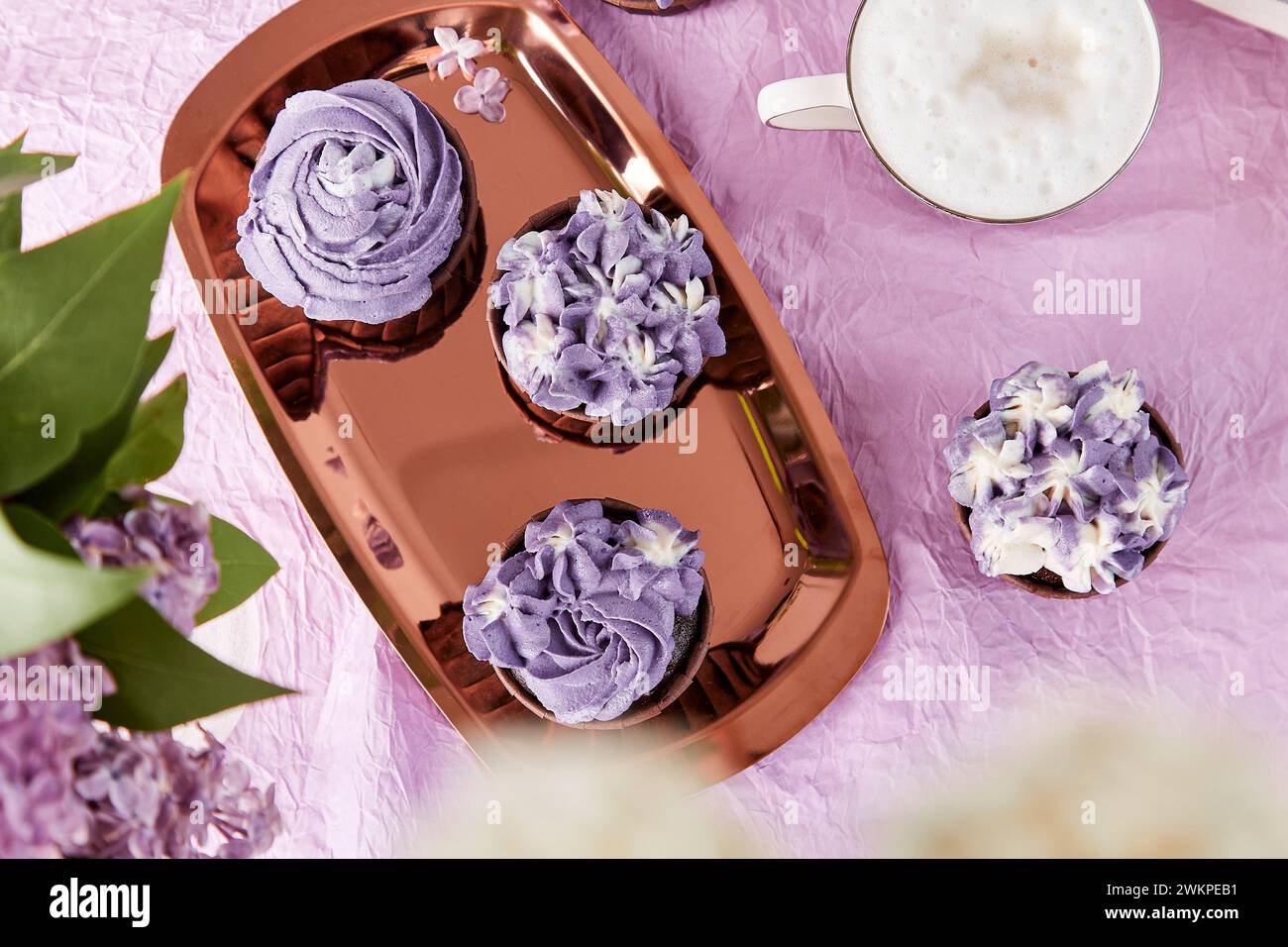 Festive aesthetic holiday table. Purple french cupcakes with cup of coffee. Desserts, coffee and lilac flowers. Feminine lifestyle. Stock Photo