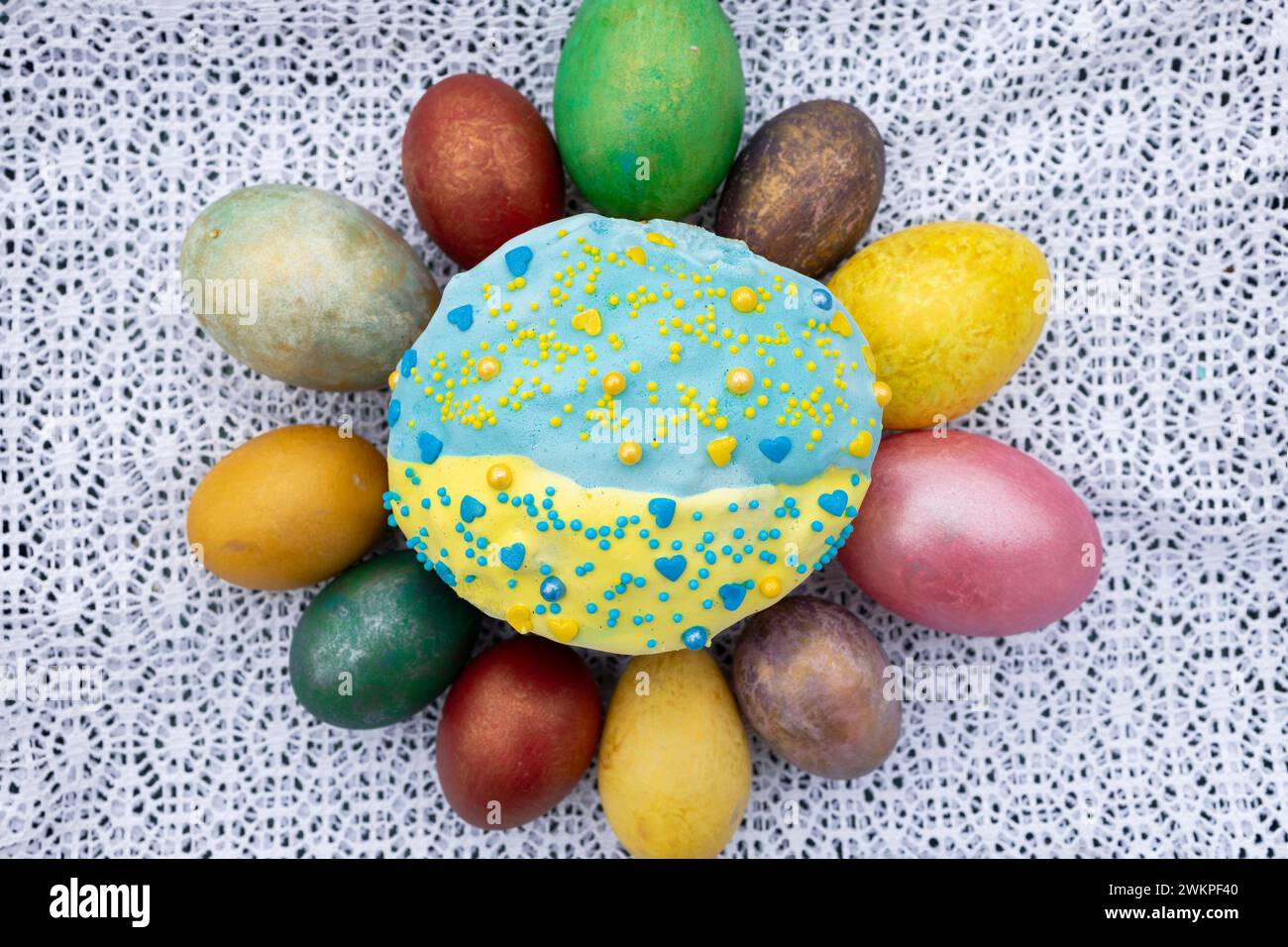 composition with multi-colored Easter eggs placed around an Easter cake sprinkled with yellow and blue glaz Stock Photo