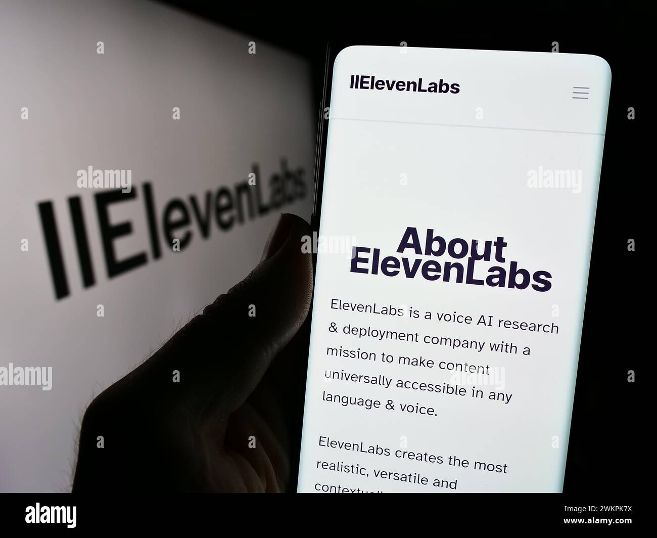 Person holding smartphone with webpage of US artificial intelligence company ElevenLabs Inc. in front of logo. Focus on center of phone display. Stock Photo