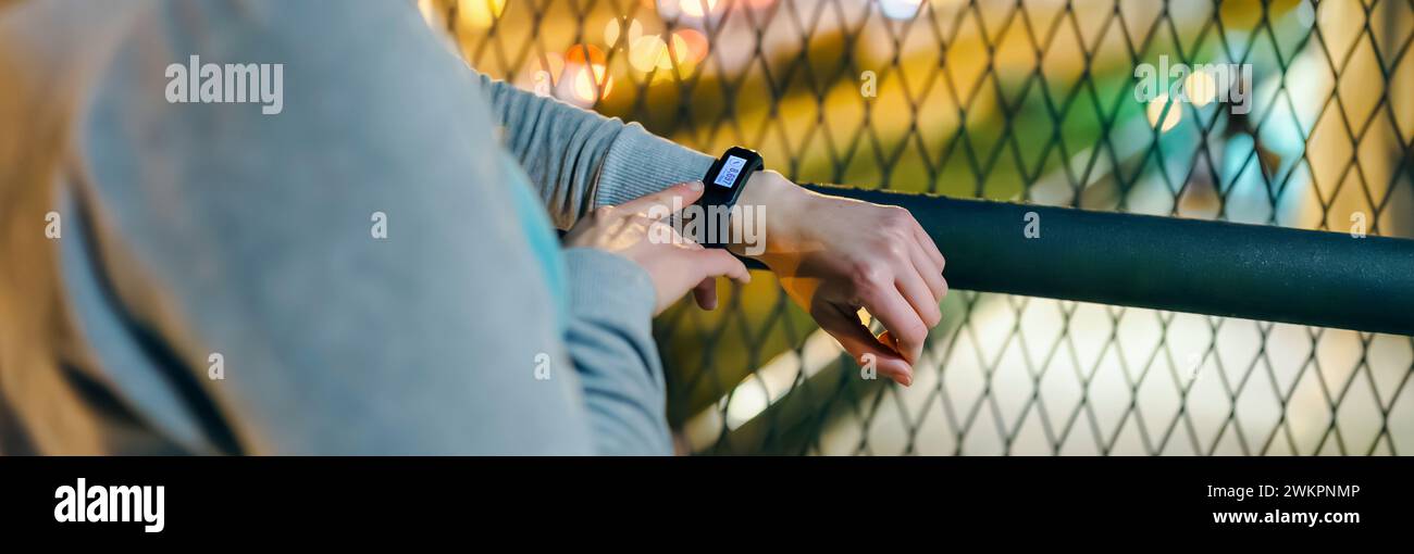 Banner of unrecognizable female hand touching digital wrist band screen to check daily step counter after walking at night on town. Woman athlete look Stock Photo