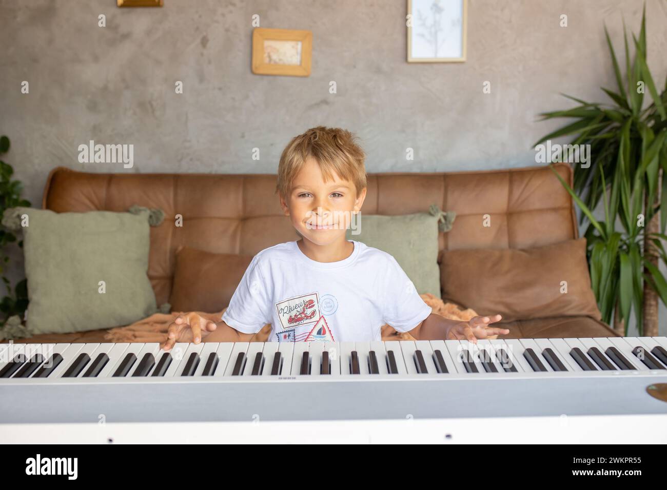Child, blond boy, playing piano at home, learning Stock Photo