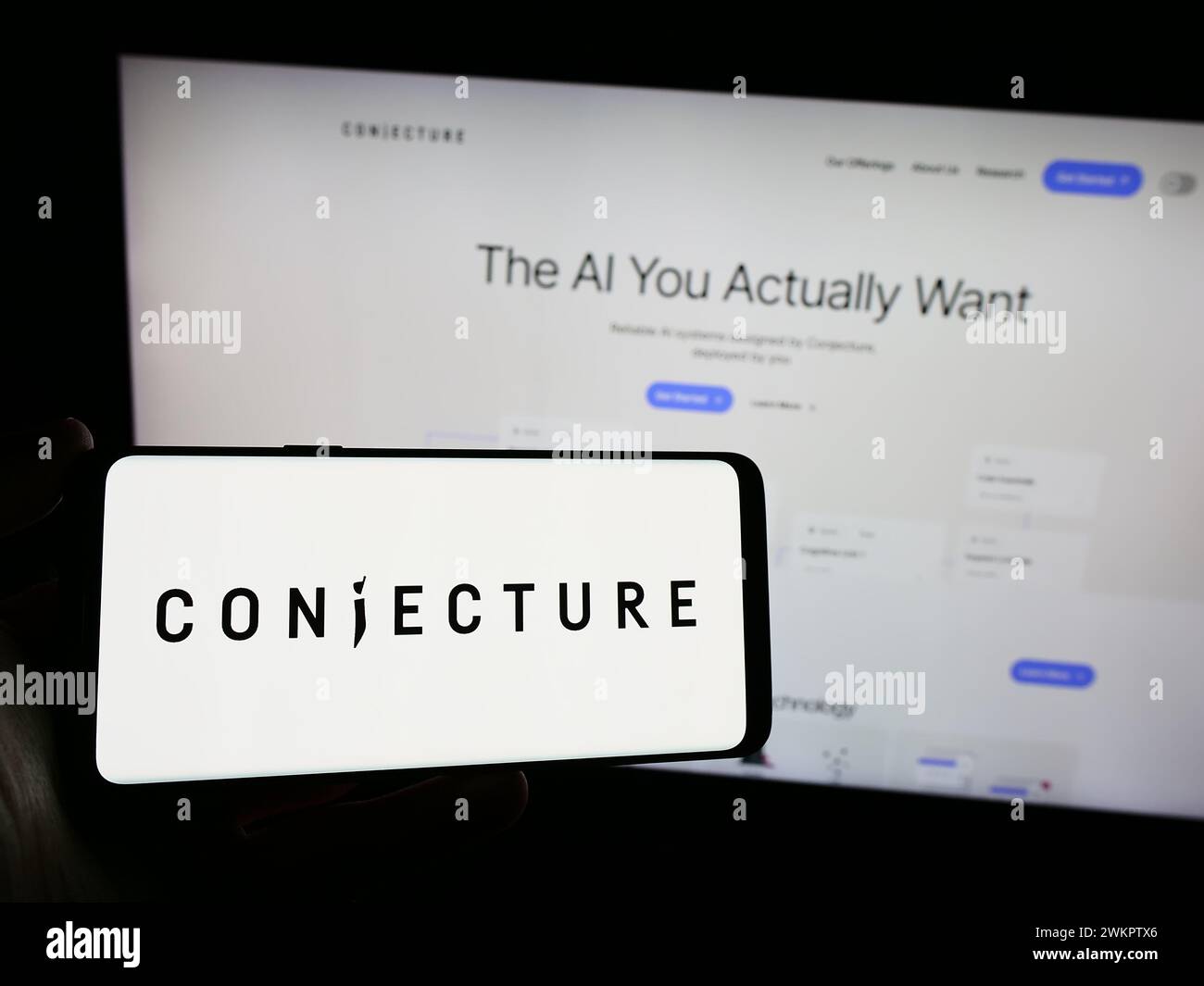 Person holding smartphone with logo of British artificial intelligence company Conjecture Limited in front of website. Focus on phone display. Stock Photo