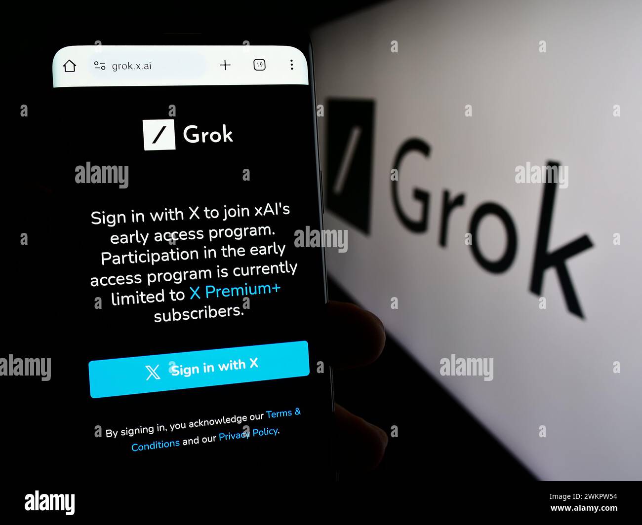 Person holding cellphone with webpage of generative artificial intelligence chatbot Grok (X.AI) with logo. Focus on center of phone display. Stock Photo