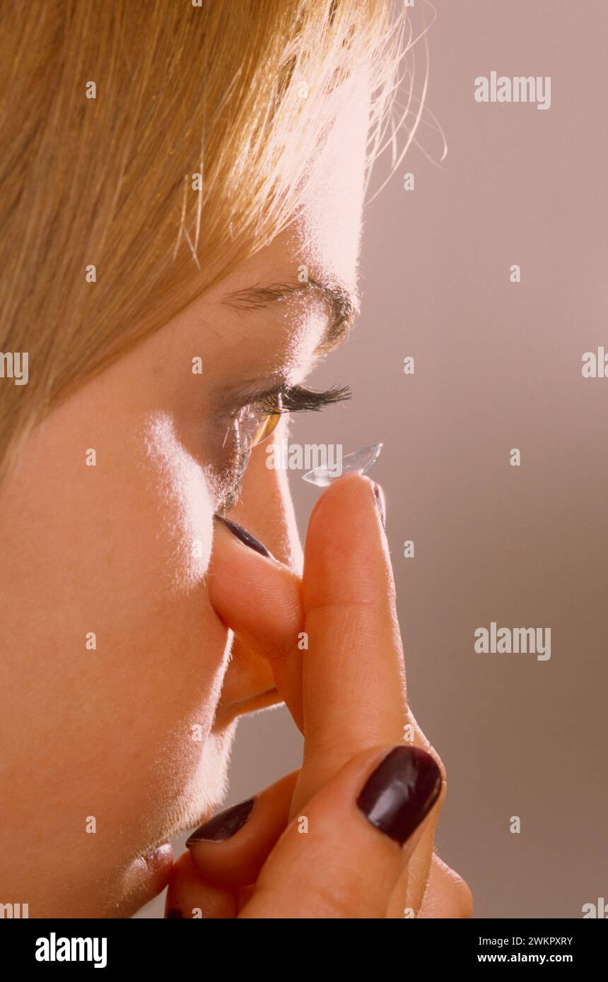 young woman putting in a contact lens with it held on the tip of her finger near her eye Stock Photo