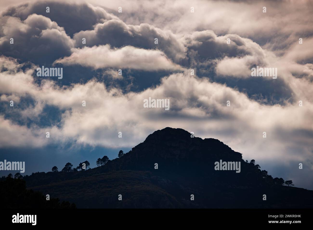 hill silhouetted under iridescent clouds in Xeraco Stock Photo