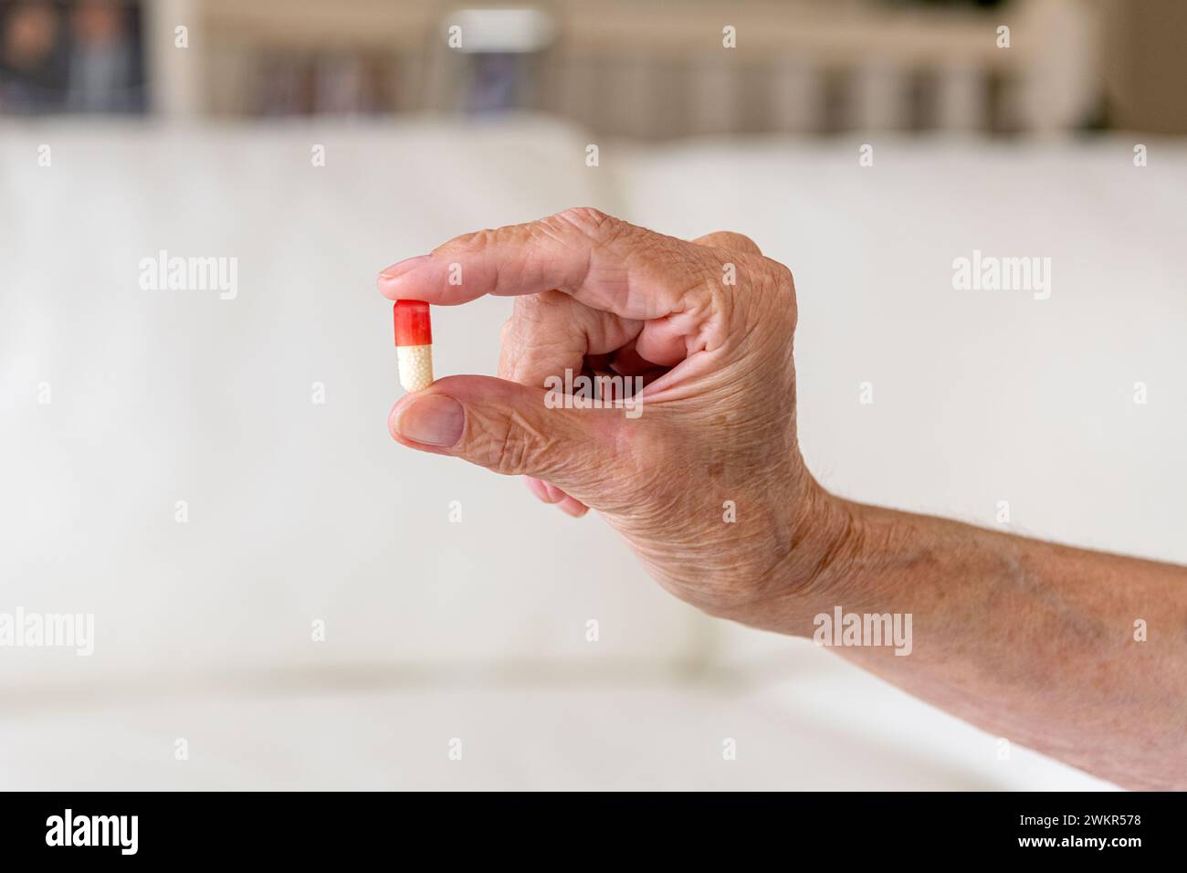 Close up of old female hand holding a red and white capsule pill in two fingers. Health care female concept Stock Photo