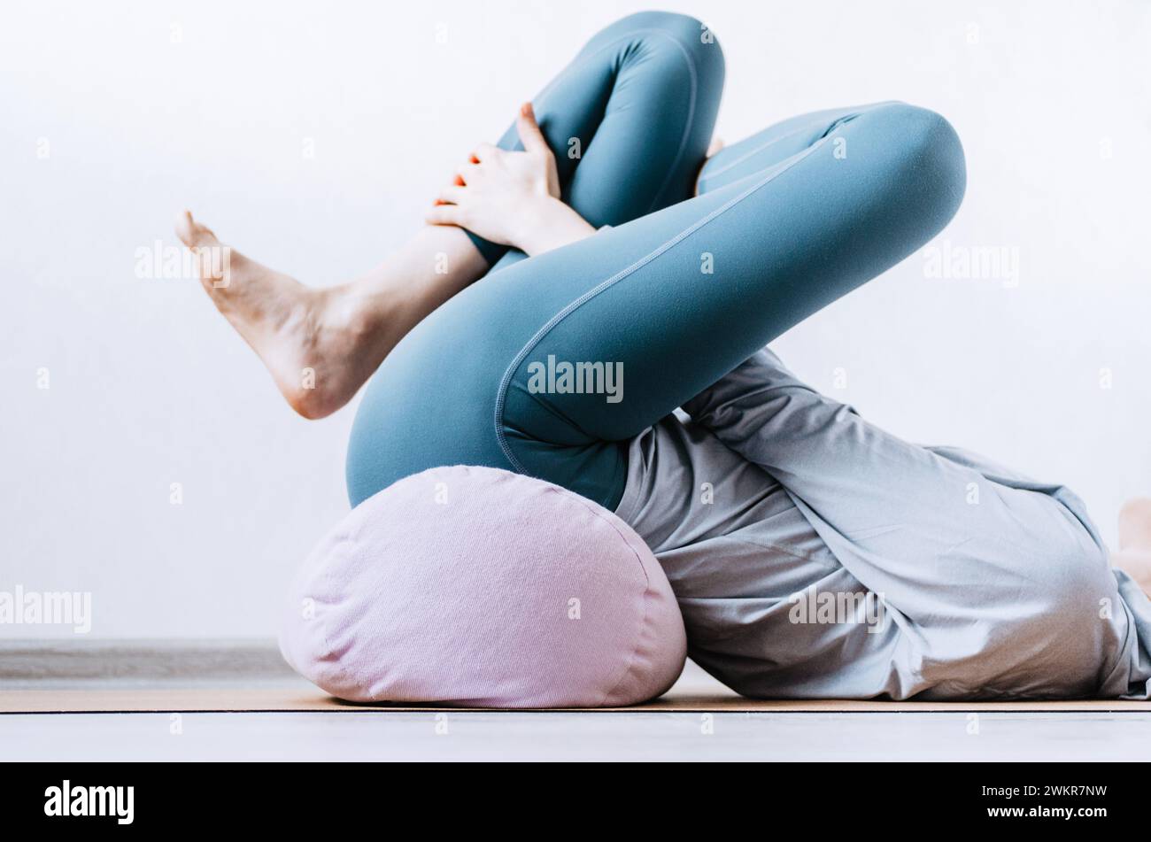 Woman doing yin yoga passive hip stretch exercises on bolster Stock
