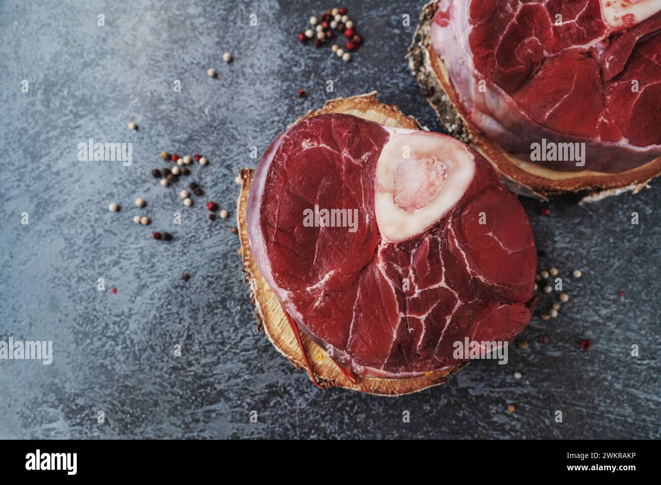 raw Ossobuco. Veal shanks Ossobuco with pepper, lemon and garlic for gremolata, typical ingredients of Italian Lombard cuisine, top view on dark backg Stock Photo