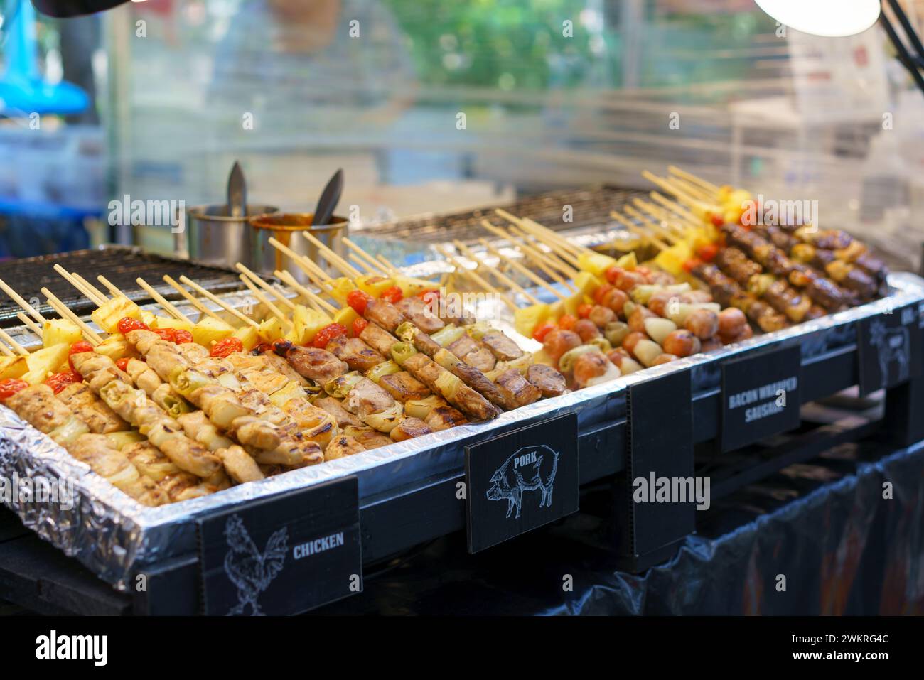 An appetizing array of grilled skewers featuring chicken, pork, and bacon-wrapped sausages, accompanied by vegetables, displayed at a street food stan Stock Photo