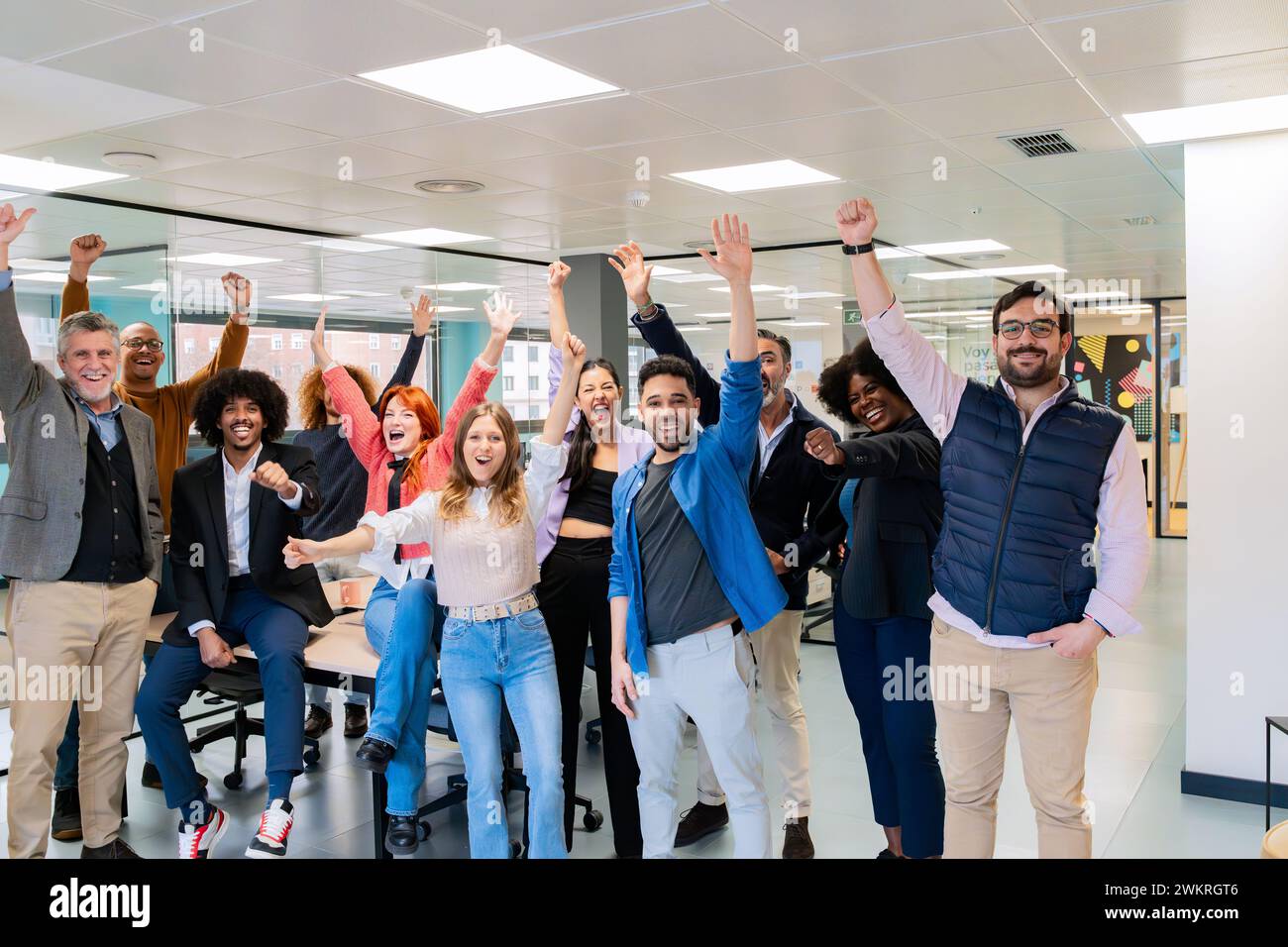 An enthusiastic team of office workers celebrating with raised arms in a vibrant coworking space.  Stock Photo