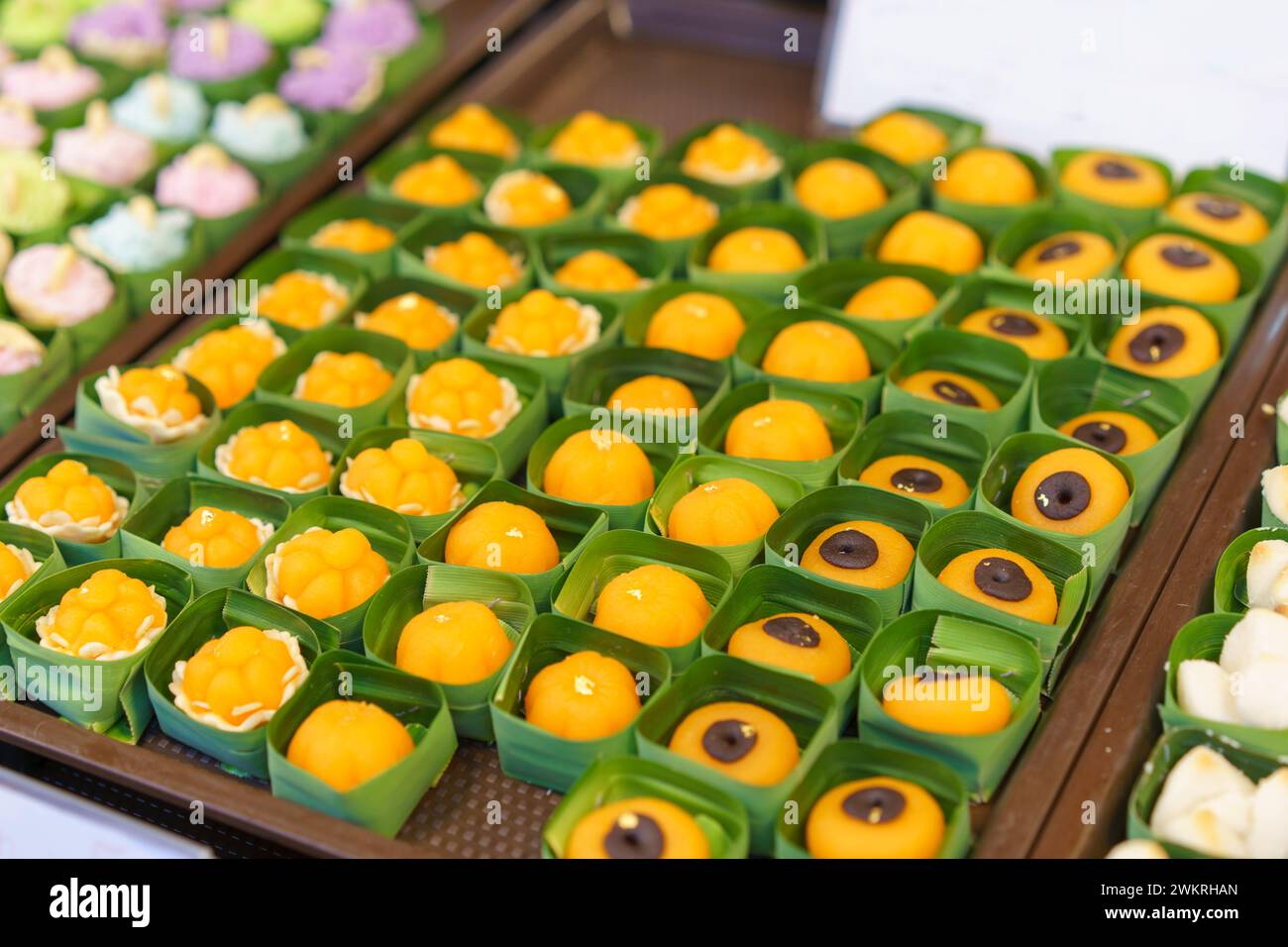Array of colorful Thai desserts, including Thong Ek and Khanom Ja Mong Got, presented in eco-friendly banana leaf cups at a street market Stock Photo