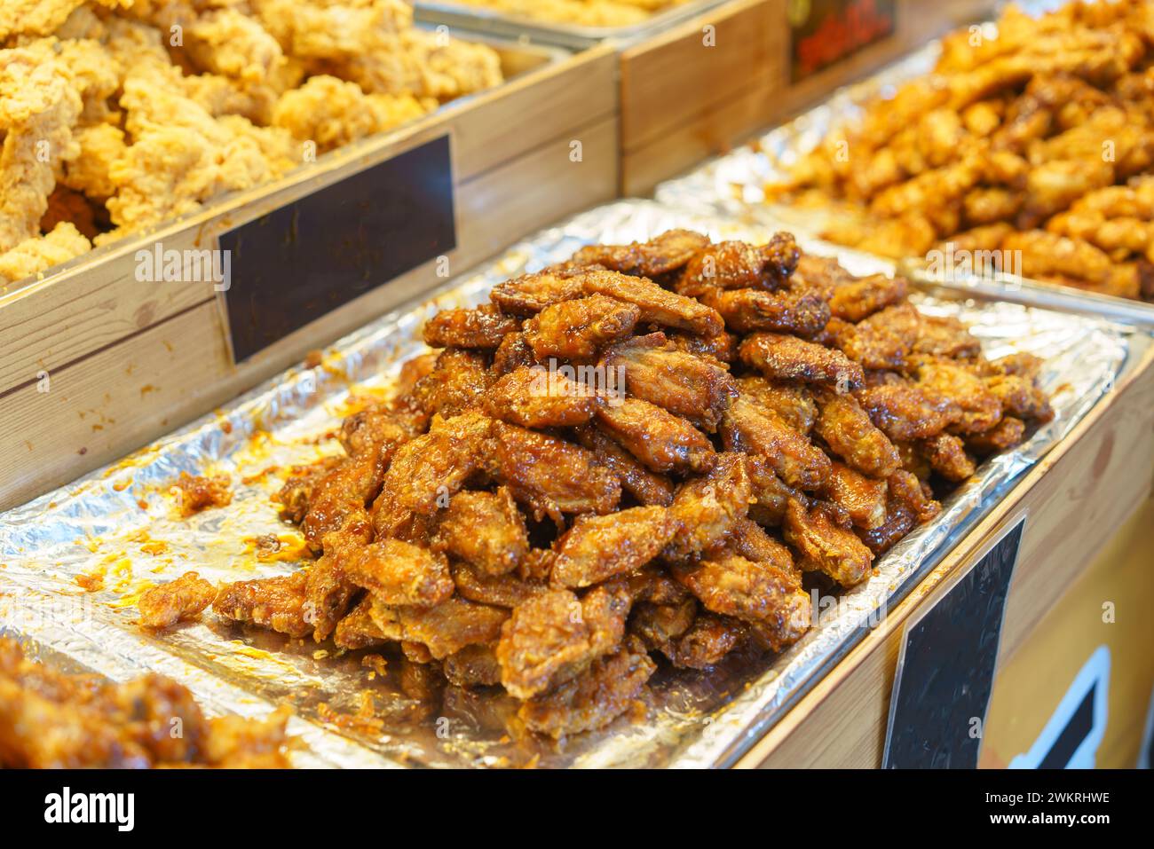 Generous portions of honey-glazed chicken wings, glistening and perfectly cooked, displayed at a food market stall Stock Photo