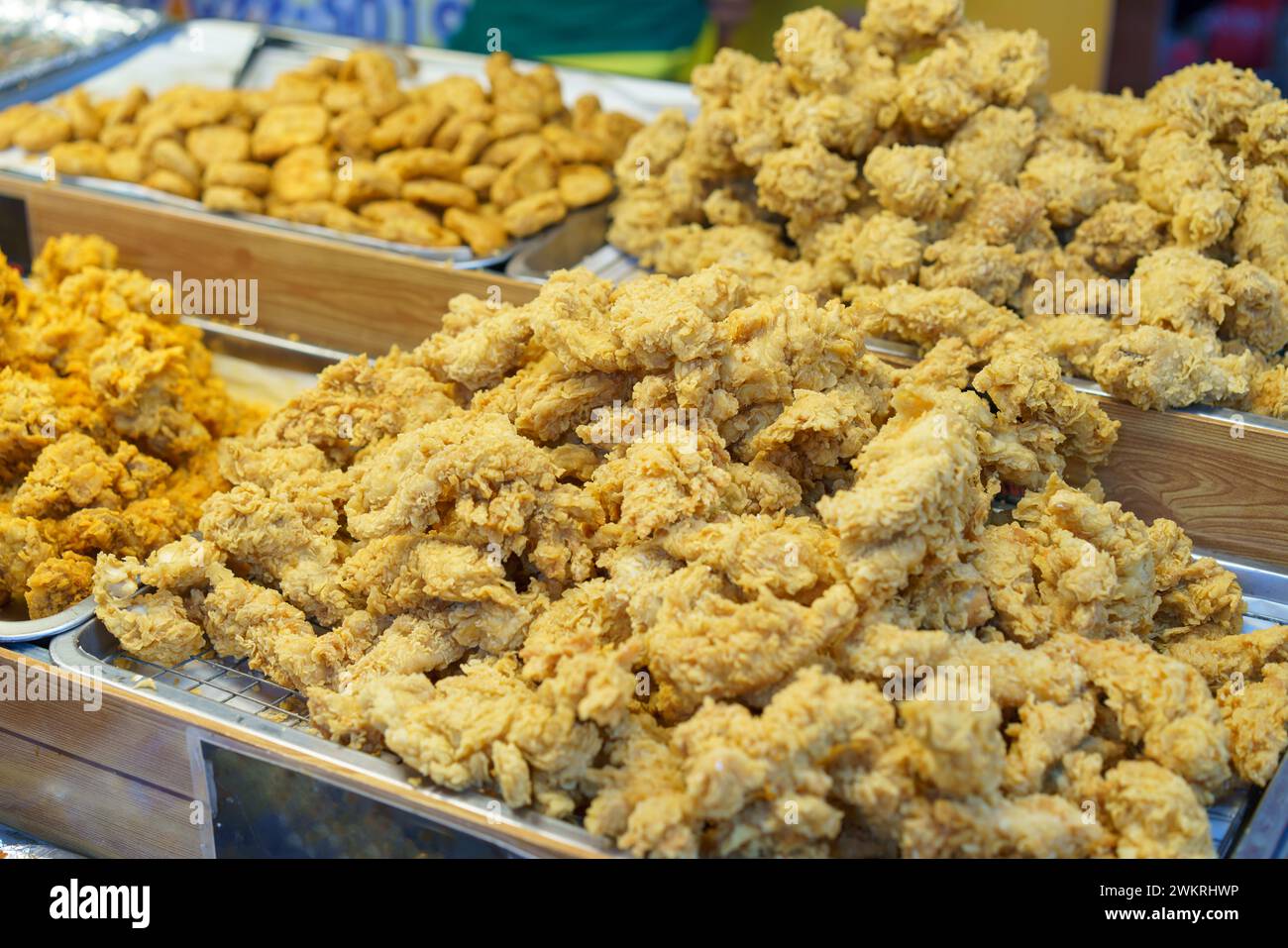 Trays filled with crispy golden fried chicken pieces, ready to be served to customers at a busy food market Stock Photo