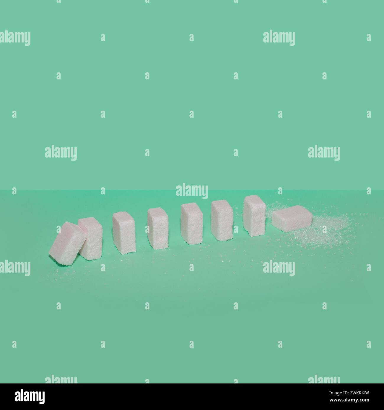 Sugar cubes as domino effect on a green background. Creative food concept. Stock Photo