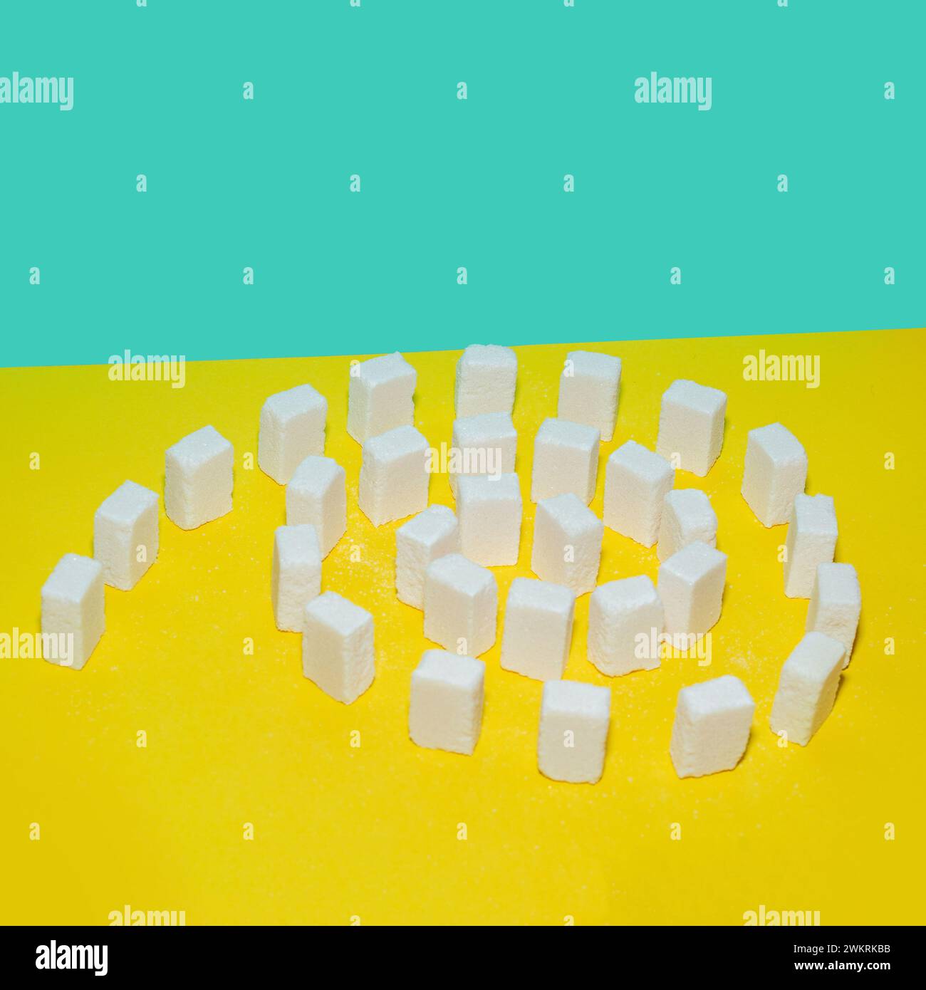 White sugar cubes on a yellow and blue background. Creative concept top view. Stock Photo