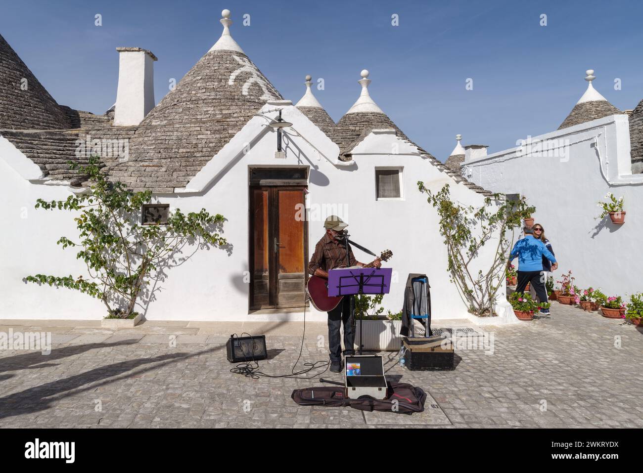 An artist busker playing on the Via Monte San Michele street with typical trulli houses in Alberobello, Italy Stock Photo