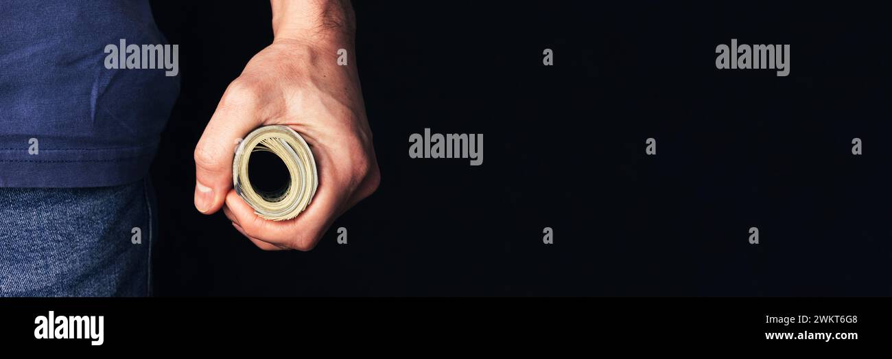 Male hand holding rolled-up money on dark background banner. Panoramic web header. Wide screen wallpaper. Stock Photo