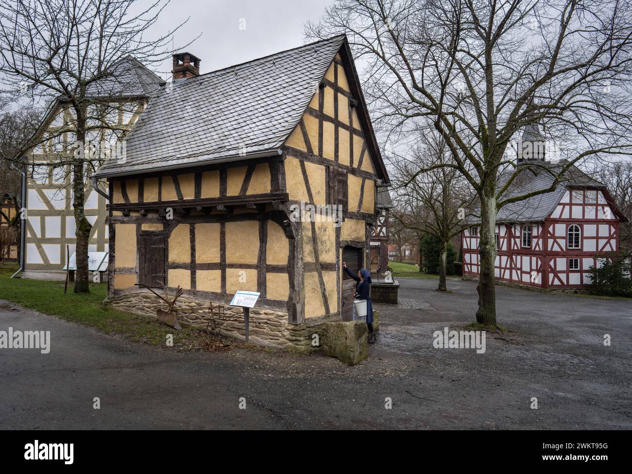 Neu Anspach, Germany. 22nd Feb, 2024. Art historian Iris von Stephanitz stands next to the oldest building in Hessenpark, the forge from Weinbach in central Hesse, which was rebuilt in 1974/75. On the right is the church from Niederhörlen, which was rebuilt here between 1974 and 1978. Hessenpark is celebrating its 50th anniversary this year. Credit: Frank Rumpenhorst/dpa/Alamy Live News Stock Photo