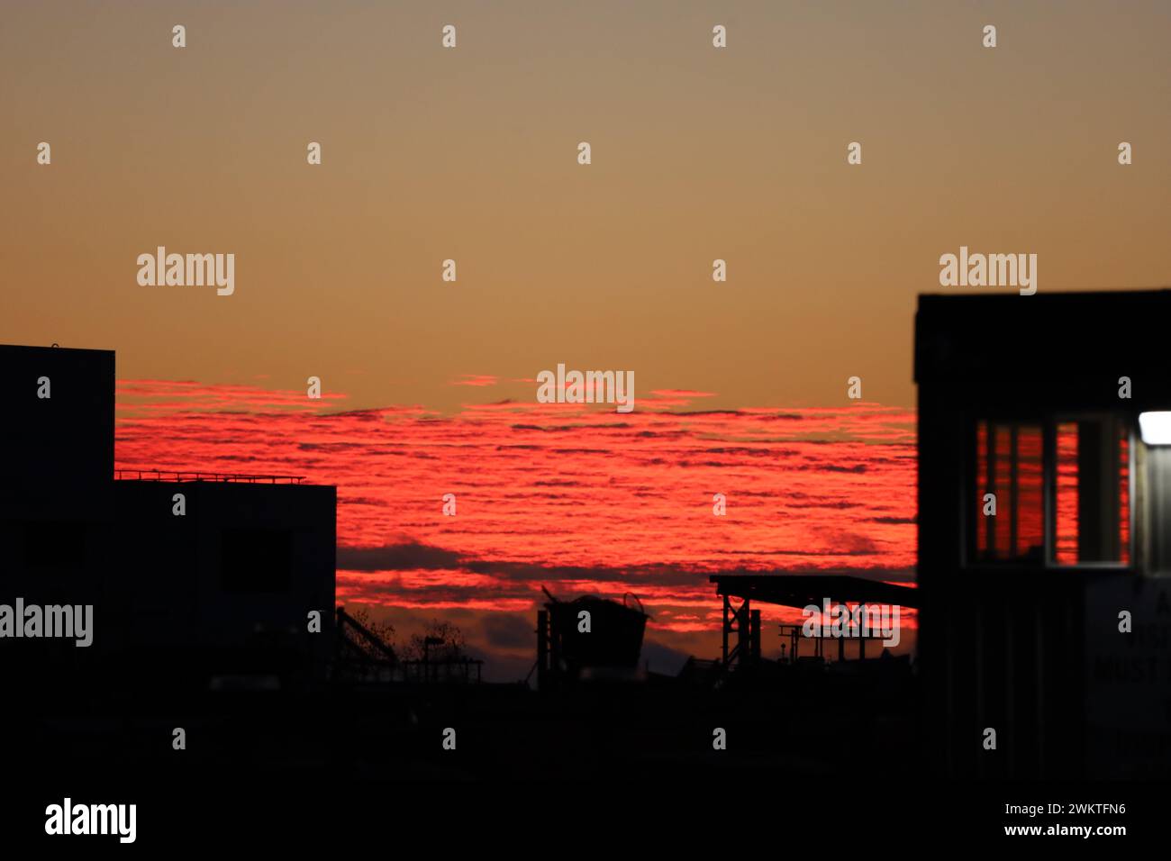 An image of various darkened structures and a red-pink winter sunrise as seen from the entrance to Tommy Thompson Park in Toronto, Ontario. Stock Photo