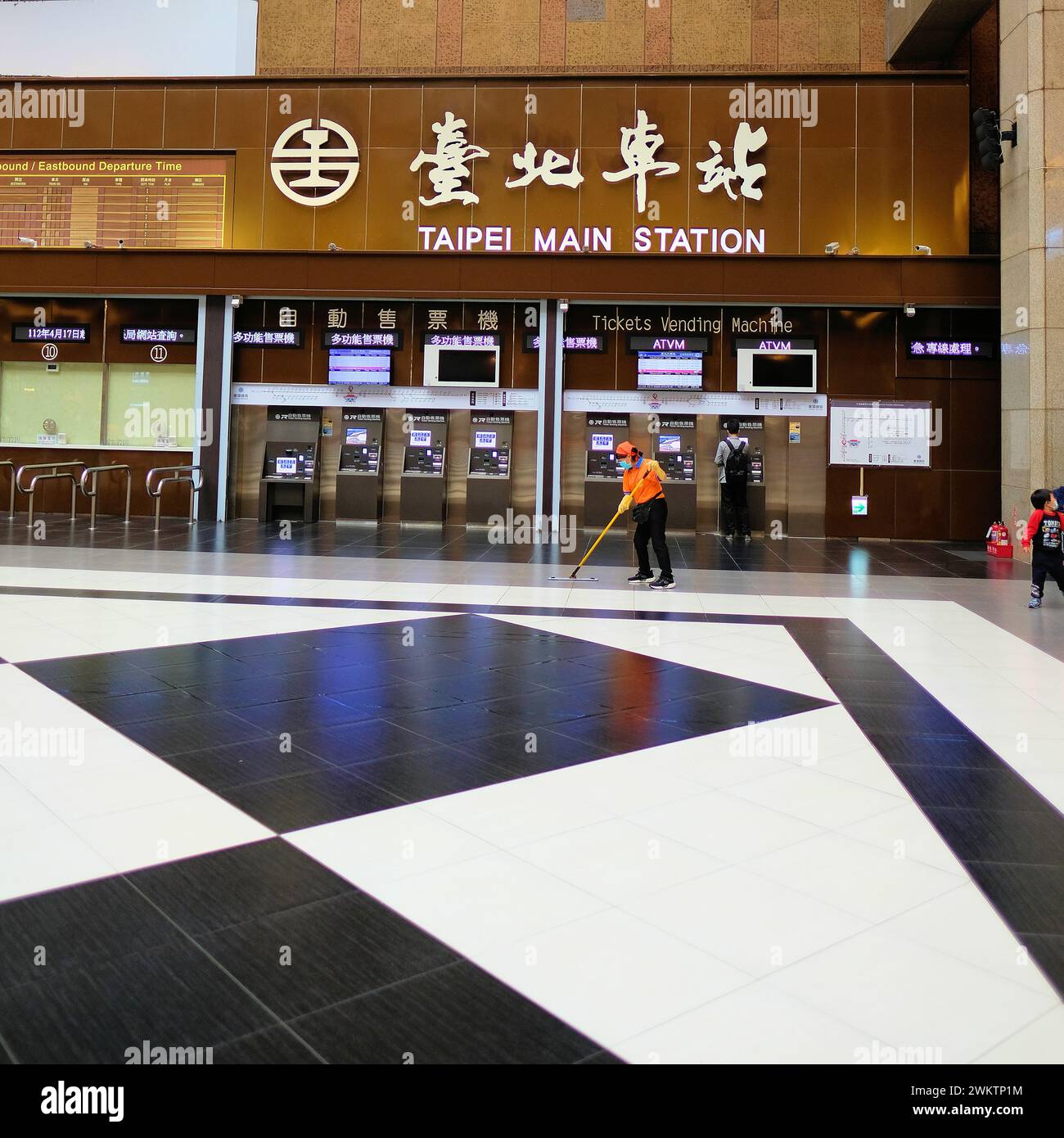 Automated ticket vending machines in the main concourse at Taipei Main Station in Taiwan; ATVM and customers, travelers, tourists, custodian sweeping. Stock Photo