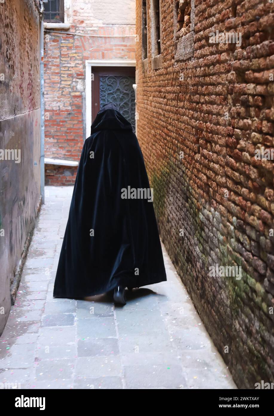 anonymous hooded stroller with black cloak dress walking through the alleys of Venice Stock Photo