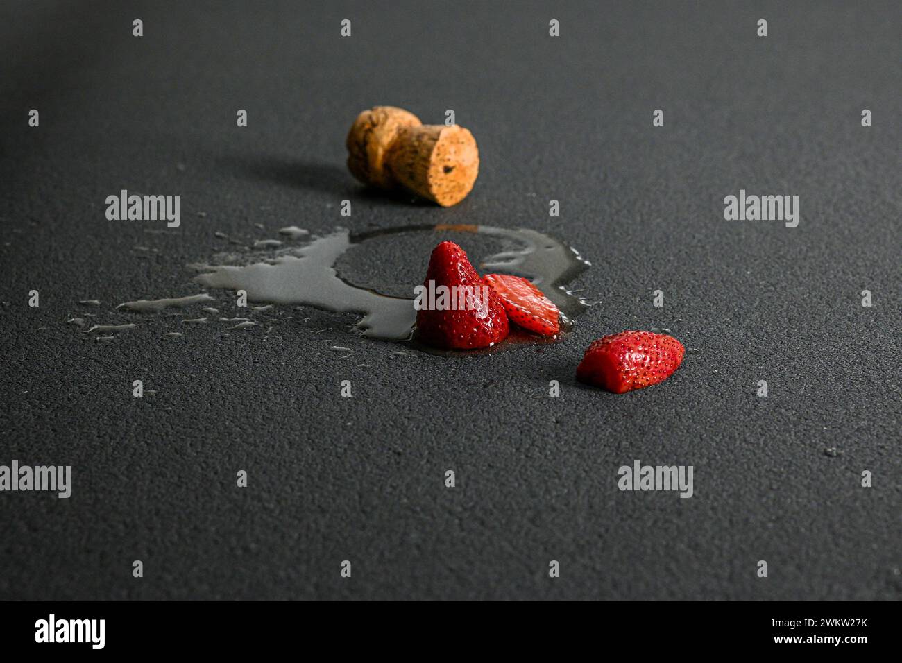 spilled wine with cork and strawberries on black background, side view. Stock Photo
