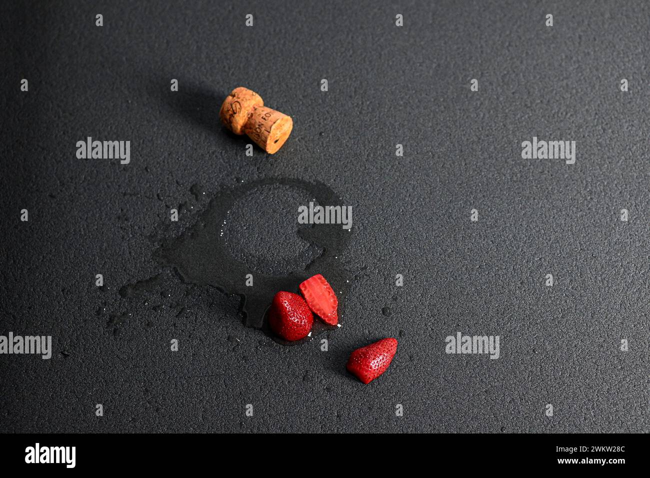 spilled wine with cork and strawberries on black background, side view. Stock Photo