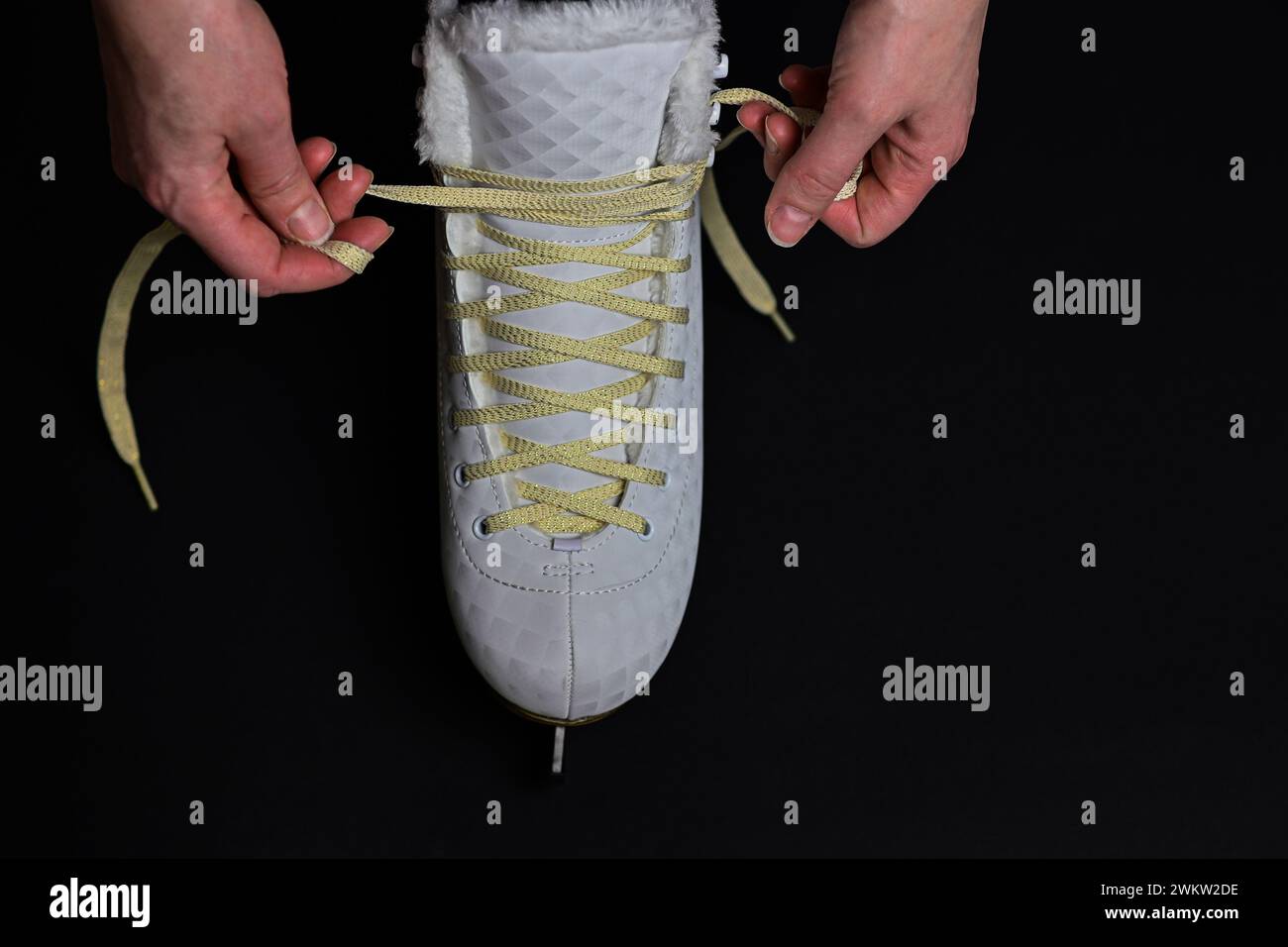 a woman laces her ice skates on a black background. Stock Photo
