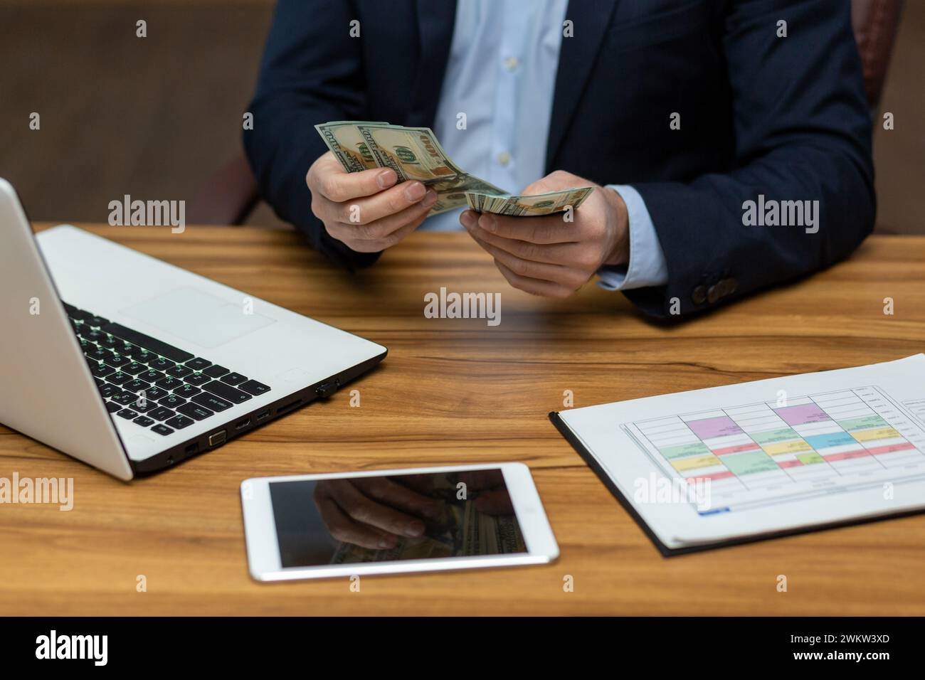 Photo concept close-up of the hand of a young man in a business suit sitting in the office at a table with gadgets, holding and counting cash dollar b Stock Photo