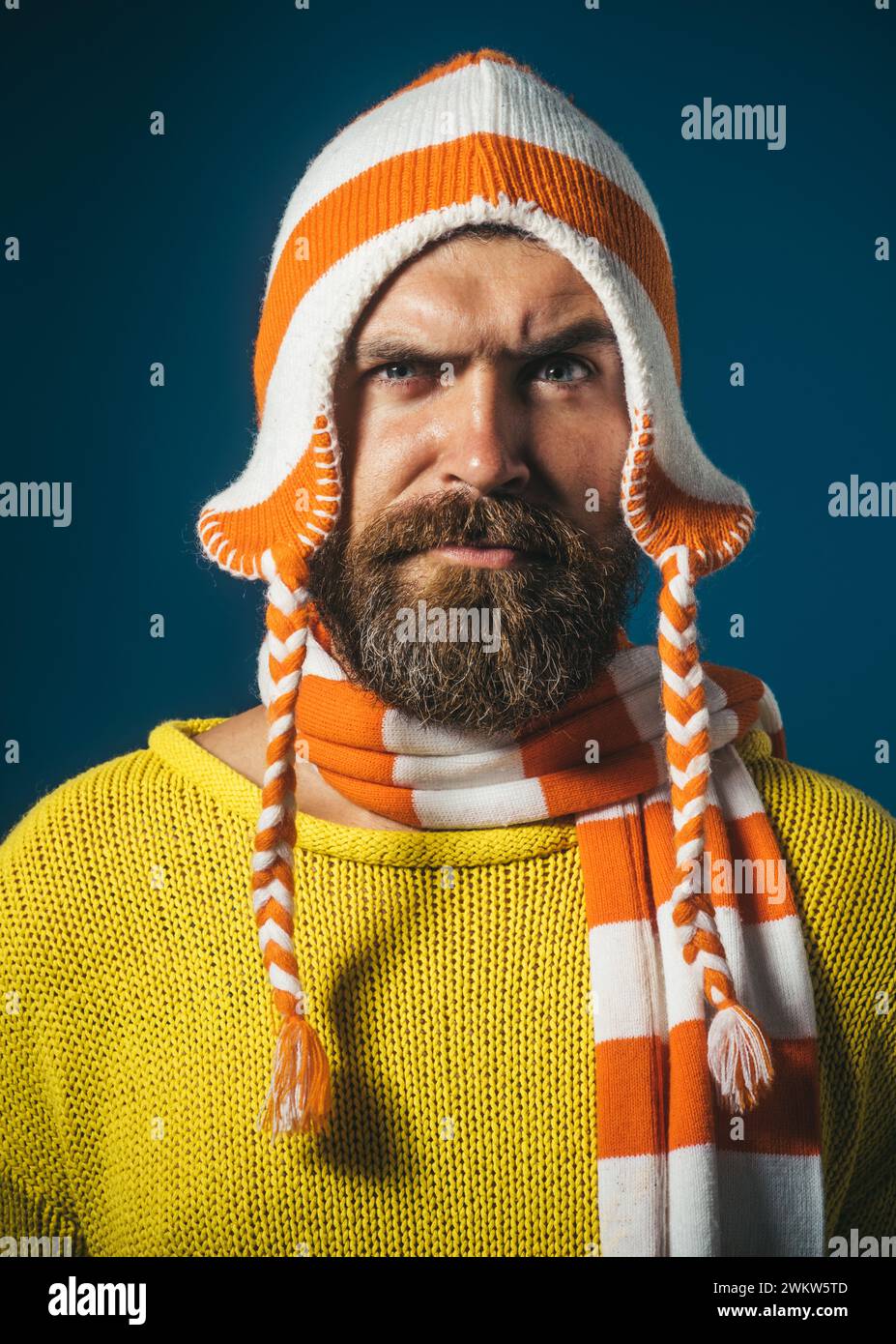Closeup portrait of serious handsome man in knitted sweater, striped hat and scarf. Stylish bearded man in casual wear. Attractive man with beard and Stock Photo
