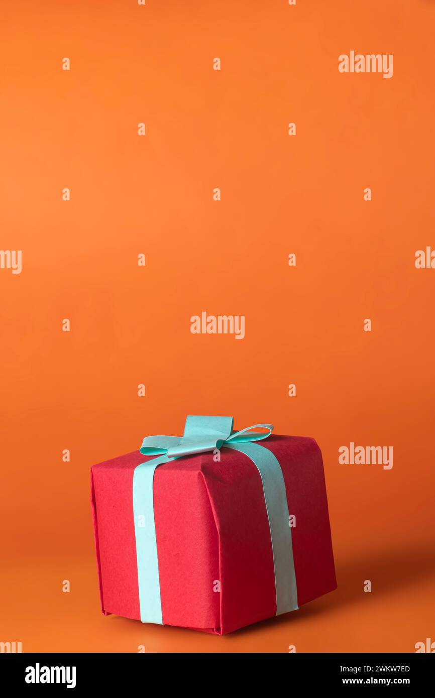 Red gift box with blue bow isolated on orange background. Copy space Stock Photo