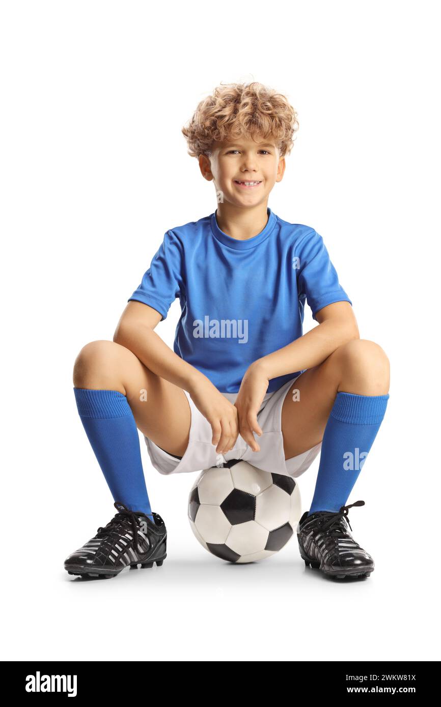 Happy boy in a sport jersey sitting on a football isolated on white background Stock Photo