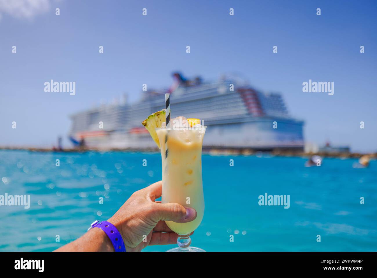 Beautiful view of man's hand holding glass of alcoholic cocktail with cruise liner in the background out of focus. Curacao. Stock Photo