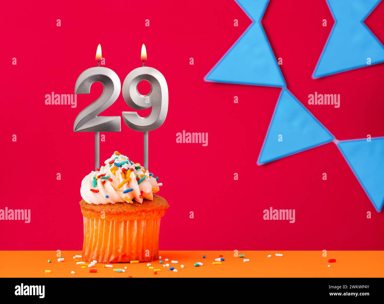 Number 29 candle with birthday cupcake on a red background with blue pennants Stock Photo