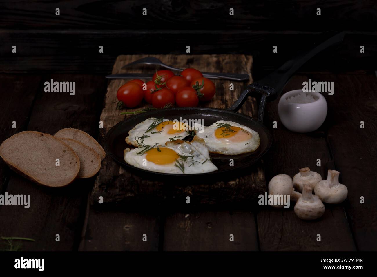 Fried eggs in a pan with vegetables and herbs on a black background Stock Photo