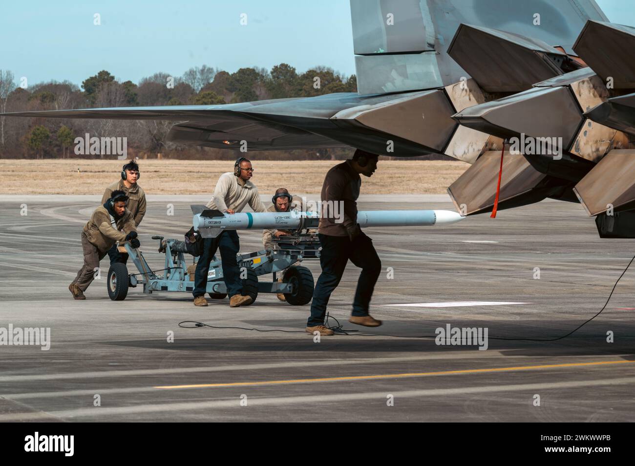 Airmen assigned to the 1st Fighter Wing load a training AIM-120 Advanced Medium Range Air-to-air missile towards an F-22 Raptor for loading at Joint Base Langley-Eustis, Virginia, Feb. 8, 2024. The 1st Fighter Wing paired with the 6th Airlift Squadron to test joint capabilities, which focused on integrated combat maneuvers and refueling operations. (U.S. Air Force photo by Airman 1st Class Ian Sullens) Stock Photo