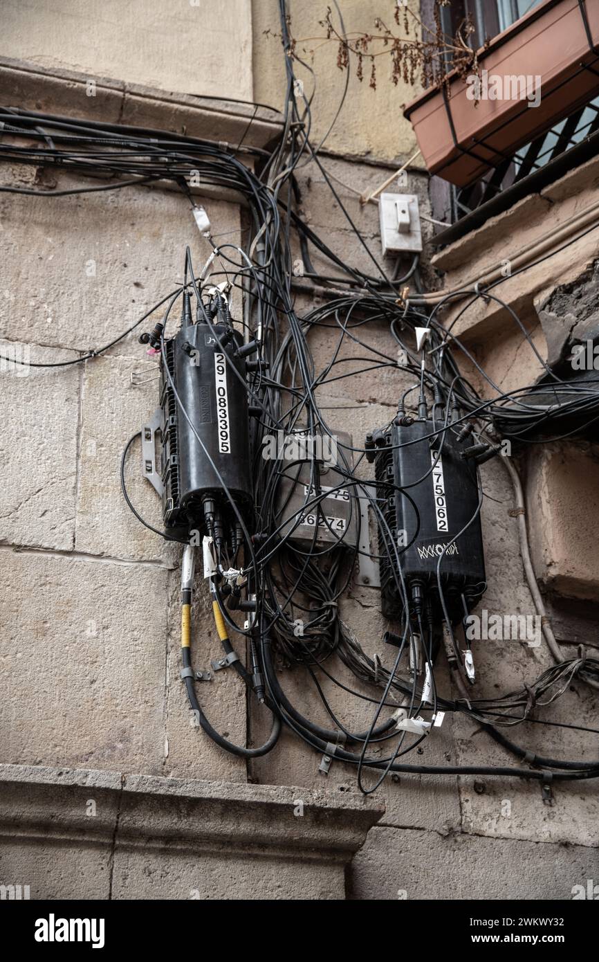 Many black telephone cables on a house wall, which end up disorganized and tangled in junction boxes. Some of the cables are labeled. This is a challe Stock Photo