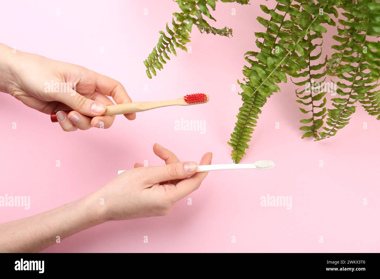 Woman holding natural bamboo and plastic toothbrushes on pink background, top view Stock Photo