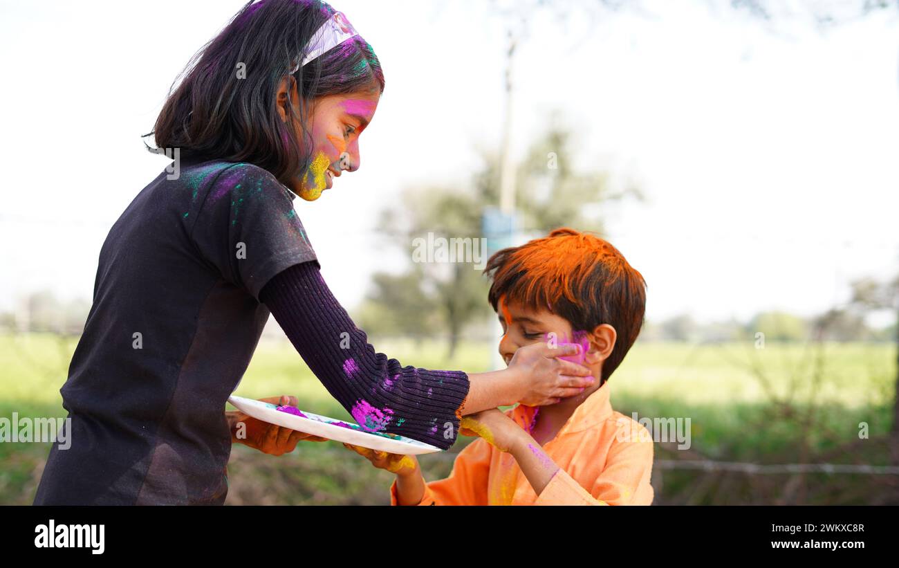 Happy Indian kids playing colours, smiling with colors on face or asian children celebrating Holi. Concept for Indian festival Holi. Bright kids smear Stock Photo
