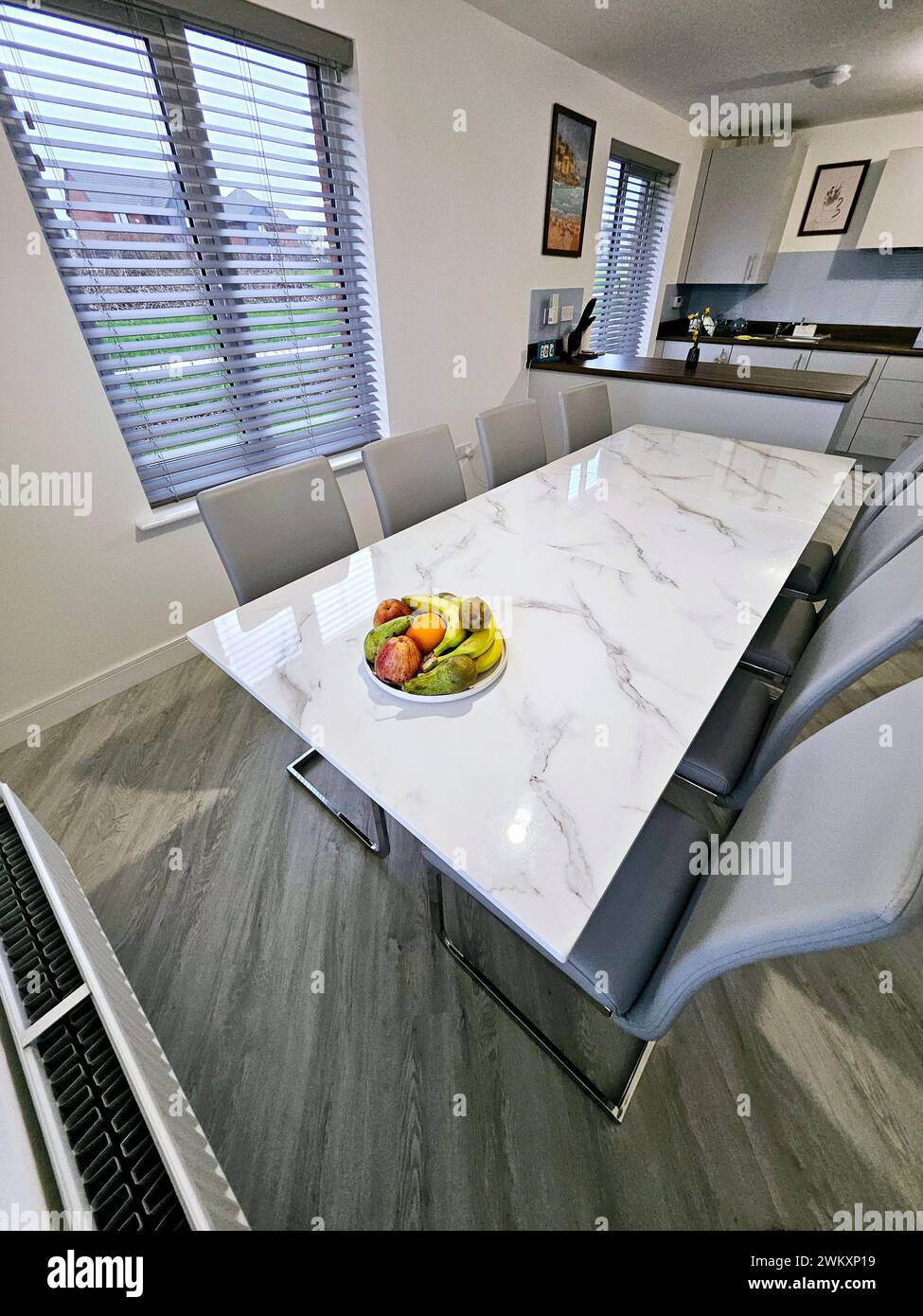 White marble table with four gray chairs and a bowl of fresh fruit on top Stock Photo