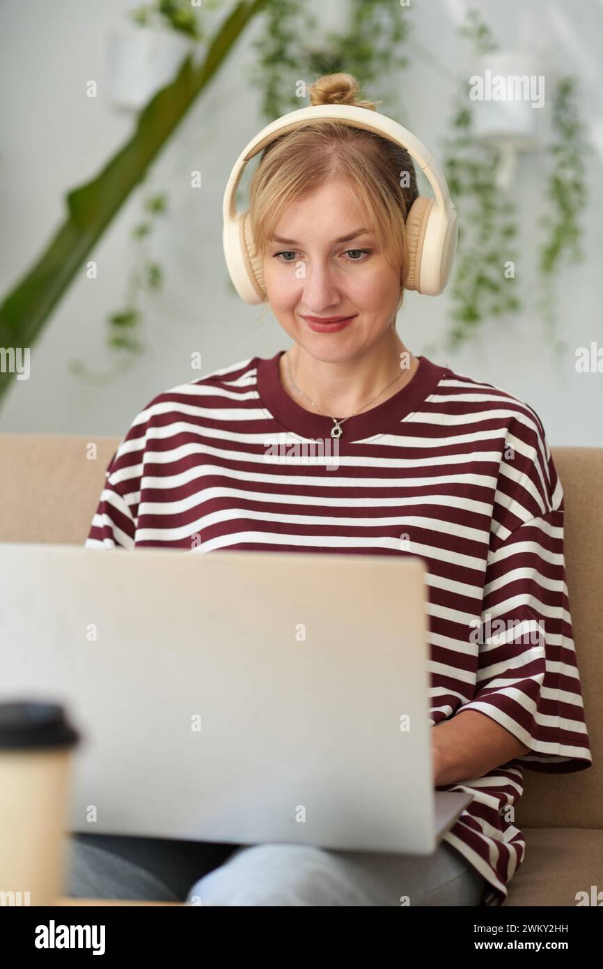 Portrait of smiling woman listening to music in headphones when coding on laptop at home Stock Photo