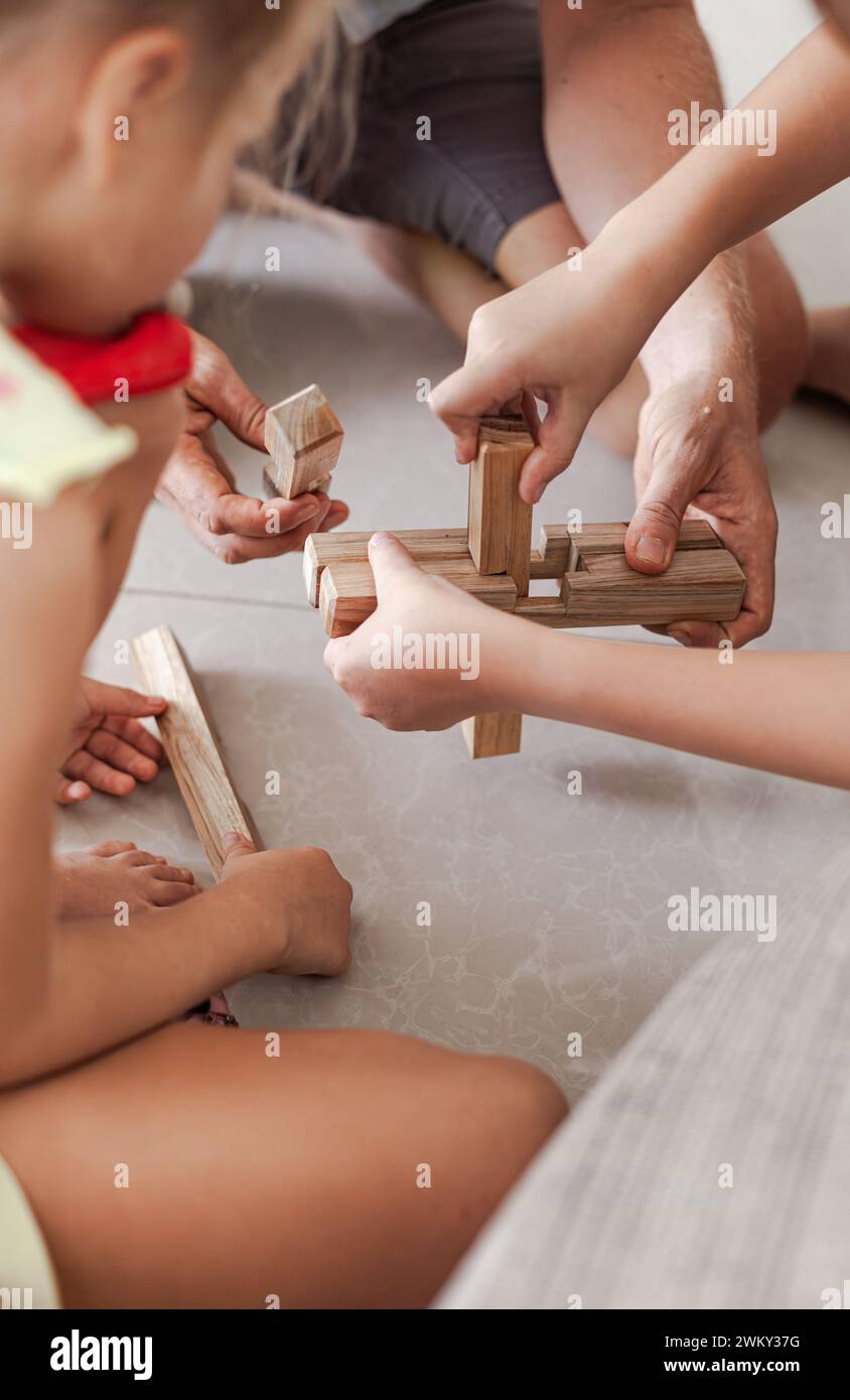 The tweens and a grownup playing wooden building blocks toys together in a light minimalist interior Stock Photo